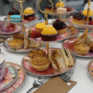 High Tea Tallawong table setup with tiered trays of desserts, finger sandwiches, tea cups, and flowers in a cozy art café setting – Colourful Wine Art Café