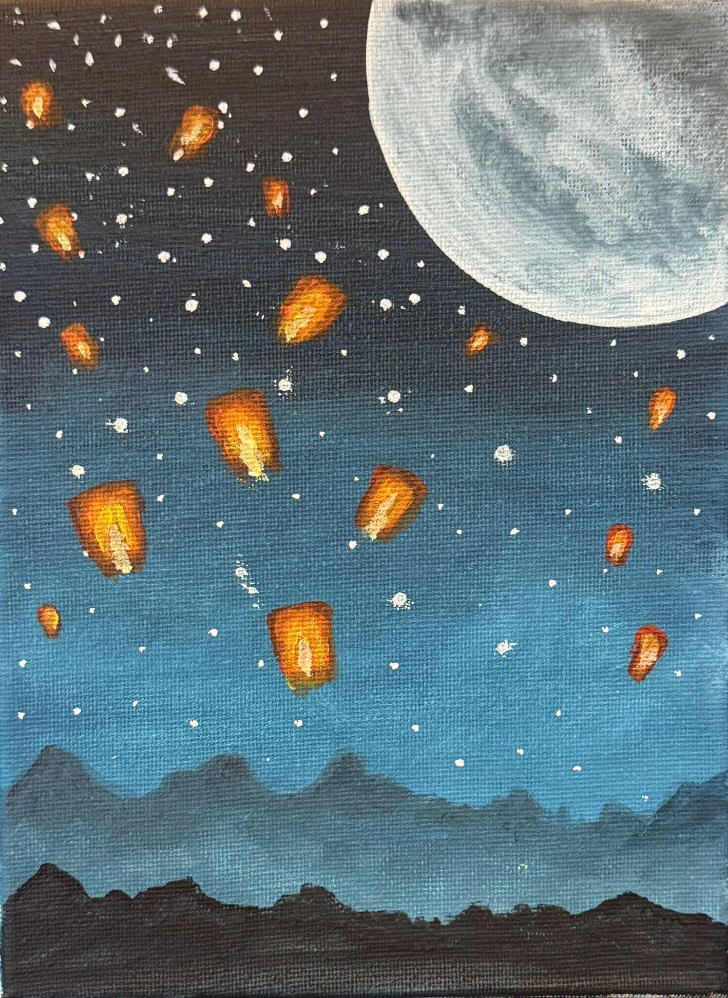 A romantic night-sky painting with glowing lanterns drifting upward against blue twilight tones, mountains in silhouette, and a soft moon, created for a Floating Lanterns Paint and Sip session.